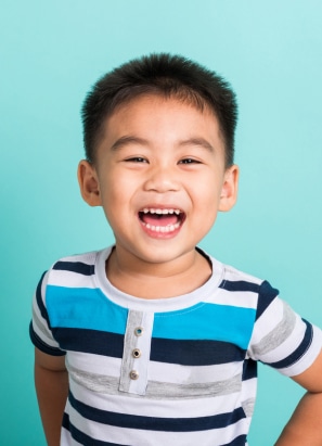 A young child with short hair wearing a striped shirt smiles joyfully against a turquoise background. No landmarks or historical buildings are visible.