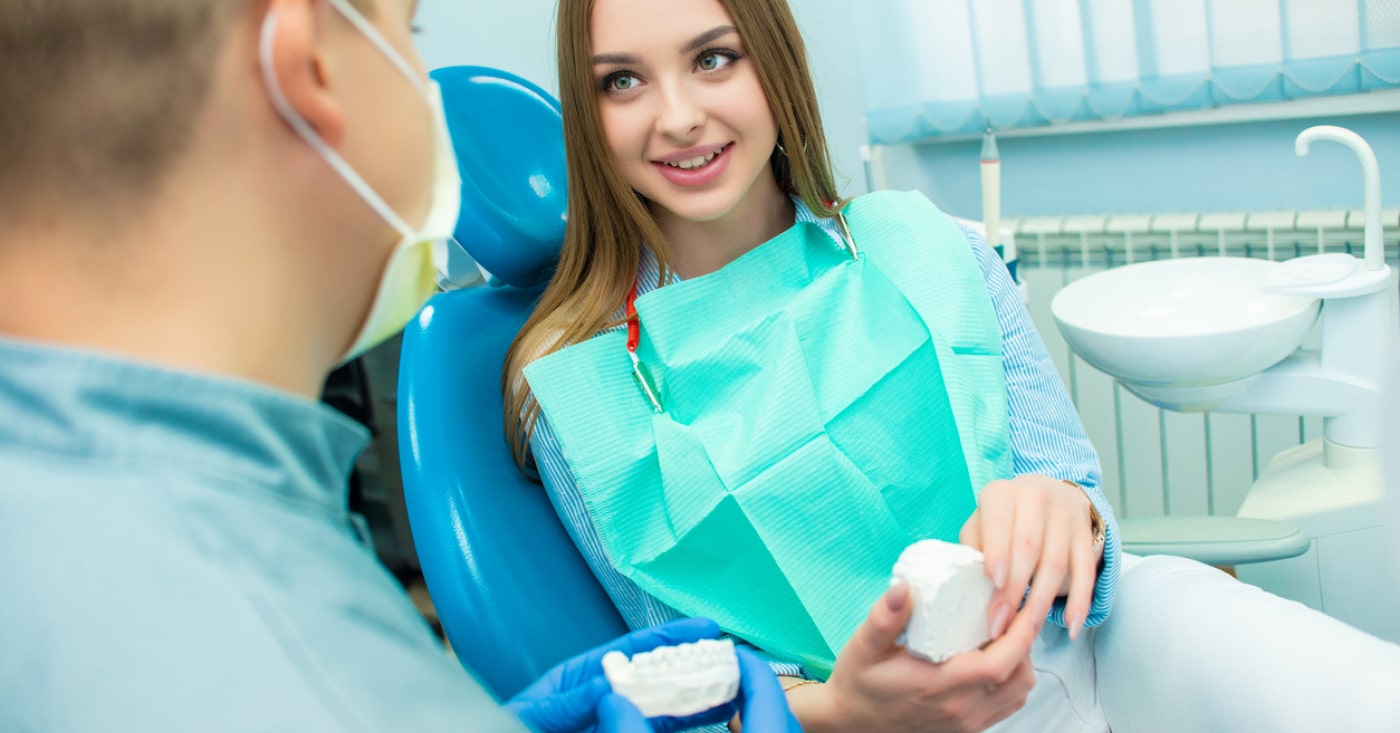 Young person with long hair sitting in dentist chair with green dental bib. 